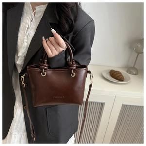 Detailed view of dark brown leather bucket bag with embossed Fashion logo and knotted handles