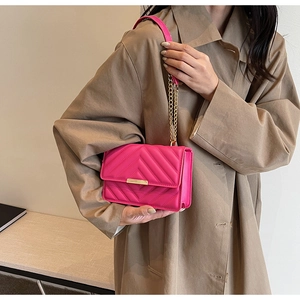 Detail of a rose red quilted crossbody bag with gold hardware worn on a khaki trench coat