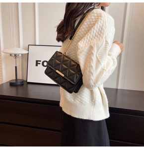 Detail of black quilted shoulder bag featuring gold chain and metallic bar closure clasp