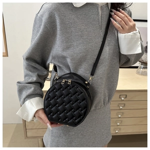 Close-up of black quilted round crossbody bag with gold zippers and leather handle
