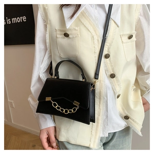Close-up of black structured leather bag with thick gold chain and crossbody strap detail