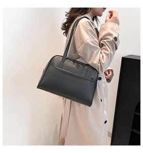 Side view of a minimalist black tote bag with slim shoulder straps on a beige coat