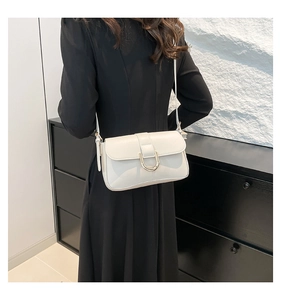 Side view of a white leather crossbody bag with U-shaped gold hardware on model