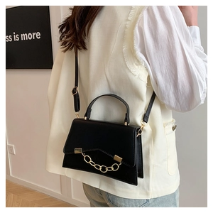 Detail of black mini box bag featuring gold chain embellishment and crossbody strap