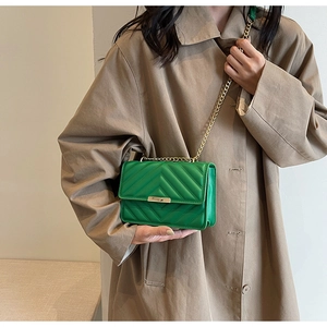 Detail of green quilted shoulder bag with gold chain strap and metallic buckle on model