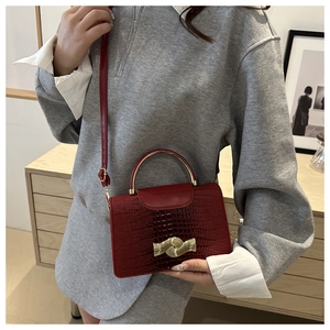 Detail of red crocodile pattern handbag featuring a gold metal handle and shoulder strap