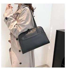 Close-up of minimalist black leather tote bag with exterior pocket on model in trench coat