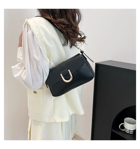 Minimalist black leather baguette bag with a gold U-shaped buckle shown on model