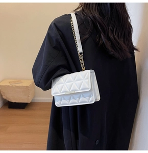 Lifestyle view of a white quilted shoulder bag with gold chain strap on a model