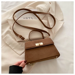 Close-up of brown suede handbag with golden twist lock and adjustable shoulder strap