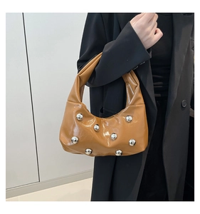 Détail du sac brillant marron caramel avec rivets sphériques argentés et blazer noir