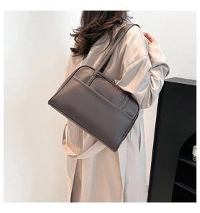 Detail of dark brown faux leather tote bag with large front pocket on a beige trench coat