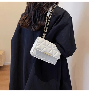 Close-up of a white quilted crossbody bag with gold chain strap on a black coat