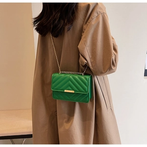 Green quilted crossbody bag with gold chain strap worn over a brown coat