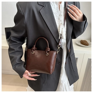 Detail of dark brown bucket bag featuring knotted handles and gold hardware accents