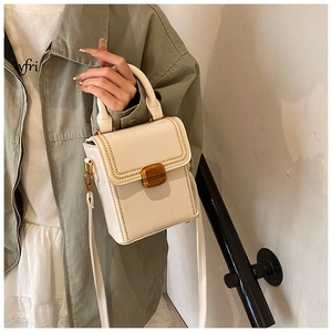 White rectangular box bag with gold metal clasp and chain trim shown on a crossbody model