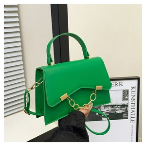 Détail du sac boîte vert avec rabat en V et une chaîne décorative en métal doré