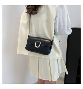 Close-up of black leather crossbody bag with a golden U-shaped buckle on a model