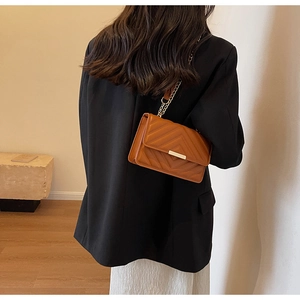 Rear view of model wearing a brown V-quilted faux leather crossbody bag with chain strap