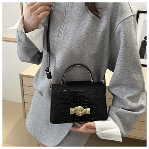 Detail of glossy black crocodile pattern handbag featuring a wavy gold metal buckle lock