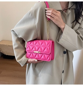 Detail of neon pink quilted crossbody bag with gold buckle on a beige trench coat