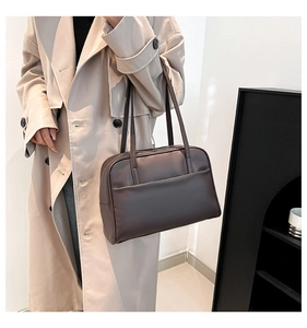 Detail of dark brown tote bag with shoulder strap paired with a beige trench coat
