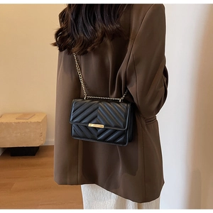 Detail of black quilted leather shoulder bag with gold chain strap on model