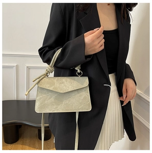 Detail of grey-green marbled handbag featuring a unique knotted handle and slim shoulder strap