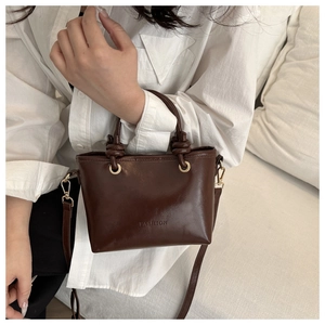 Detail of dark brown mini tote bag with knotted handle and embossed fashion logo
