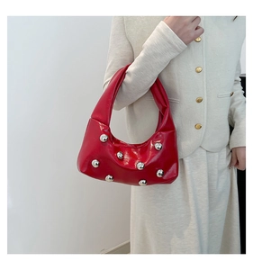 Détail d'un sac porté épaule en cuir verni rouge avec des rivets sphériques argentés