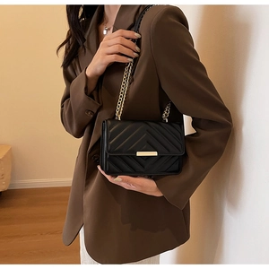 Detail of black quilted crossbody bag with gold buckle and chain on a stylish model