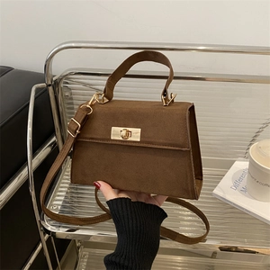 Sac à main en daim marron foncé avec fermoir doré sur un support acrylique transparent