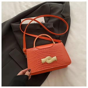 Macro shot of orange crocodile embossed texture and golden metal handle on handbag