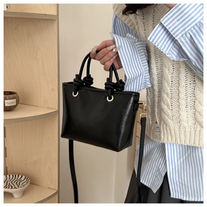 Detail of black leather bucket bag with knotted handle and golden buckle hardware