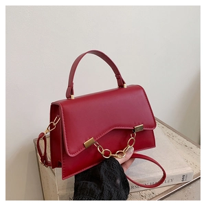 Détail du sac rouge en cuir avec rabat ondulé et décoration de chaîne dorée