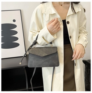 Detail of dark grey retro crossbody bag worn with a white trench coat in urban style