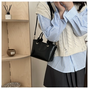 Detail of minimalist black matte leather crossbody bag with gold ring and fashion embossing