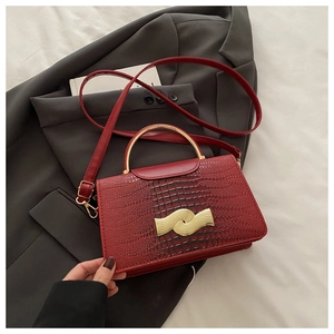 Detail of red crocodile textured handbag with golden semi-circular metal handle and strap