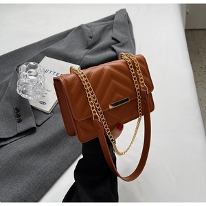 Detail of a brown quilted leather crossbody bag with V-shaped stitching and gold metal buckle