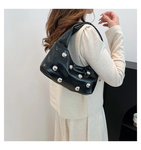 Détail macro du sac hobo noir brillant avec des rivets argentés et finition métallique