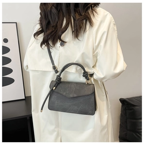 Detail of grey crossbody bag with knot handle worn over an oversized beige trench coat
