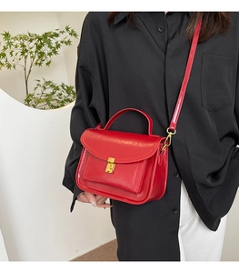 Detail of red leather crossbody bag with gold buckle and adjustable shoulder strap