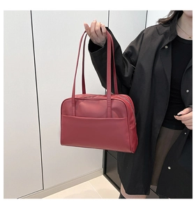 Minimalist dark red tote bag with long shoulder strap worn by a model in casual grey clothes