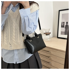 Model wearing a black leather trapezoid bucket bag with knotted handle and gold hardware