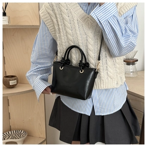 Detail of a black mini tote bag with knotted handle and golden hardware on a wooden shelf