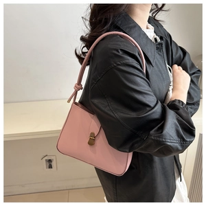 Side view of a pink minimalist leather underarm bag with gold lock on a female model