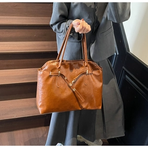 Brown leather tote bag featuring oil-wax texture and strap detail on a wooden staircase