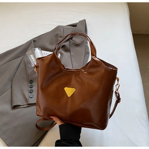 Close-up of vintage brown leather bucket bag with gold triangular plaque and dual handles