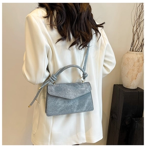 Gray-blue matte rectangle crossbody bag with unique knotted handle on a modern model