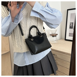 Detail of a black glossy mini bucket bag with cylindrical knot handle and gold hardware